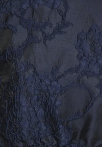Marineblaues Gewebe mit floraler Stickerei in unterschiedlichen Texturen. Das Design zeigt erhabene, filigrane Muster vor einem glatten Hintergrund.