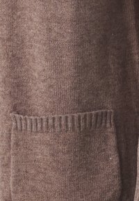 Pull en maille marron avec une texture douce, comportant une poche bien visible et des accents côtelés au niveau de l'ourlet. Le matériau semble épais et douillet.