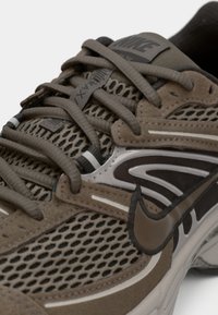 Καφέ αθλητικό παπούτσι με σχεδίαση από δίχτυ, σουέντ λεπτομέρειες και ασημί μεσαία σόλα. Τα κορδόνια και η γλώσσα διαθέτουν υφή από καουτσούκ με λογότυπο.