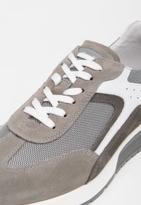 Sneaker in suede grigio e mesh con lacci bianchi, caratterizzata da un design pulito e una parte superiore testurizzata. Contrasto di colori distintivo in grigio e bianco.