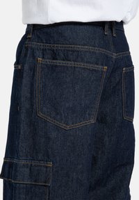 Tmavomodré denimové cargo nohavice s oranžovým prešitím. Funkcie zahŕňajú bočné vrecká, viacero zadných vreciek a uvoľnený strih.