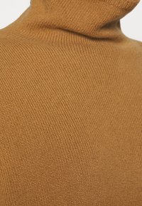 Brązowy sweter z golfem, o miękkiej teksturze i prążkowanym wzorze, podkreślający gładkie, ciągłe linie oraz wygodne dopasowanie.