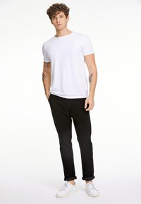 Camiseta blanca de manga corta combinada con pantalones negros y zapatillas blancas. Ajuste casual, tejido suave y dobladillos enrollados en los pantalones.