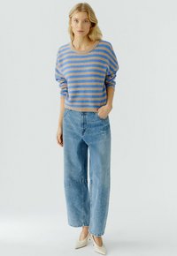 Gestreepte trui in blauw en tan, losse pasvorm met een ronde halslijn. Gepaarde met lichtgewassen, wijde jeans en beige schoeisel.