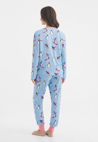 Modrý pyžamový set s potiskem tučňáka lyžujícího. Dlouhé rukávy a kalhoty s růžovými manžetami na kotnících. Měkká tkanina, volný střih a hravý design.