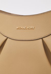 Béžová kabelka z umělé kůže s skládacím designem, se zlatým logem "MICHAEL KORS" a hladkým povrchem s prošívanými detaily.