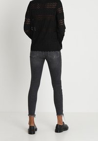 Musta pitsipaita, jossa on teksturoitu muotoilu, yhdistetty harmaisiin slim fit -farkkuihin, joissa on risaiset helmat, ja mustiin kenkiin. Näkyy takaapäin.