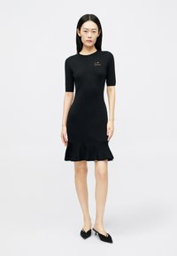 Vestido preto de algodão com corpete ajustado e barra rodada com babados, com mangas curtas e um pequeno logótipo dourado no peito.