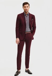 Bordowy garnitur o slim-fit, teksturowanej tkaninie i z wyłogami, połączony z koszulą w wzory oraz brązowymi skórzanymi mokasynami.