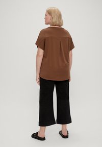 Smeđi kratki rukavi top s naborom na leđima, uparen s crnim širokim hlačama do gležnjeva. Outfit dopunjuju crne sandale.