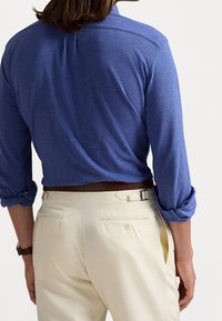 Blå skjorta med långa ärmar och uppvikta ärmar, kombinerad med krämfärgade byxor med bakfickor och bältesdetalj. Bekväm passform och texturerat tyg.