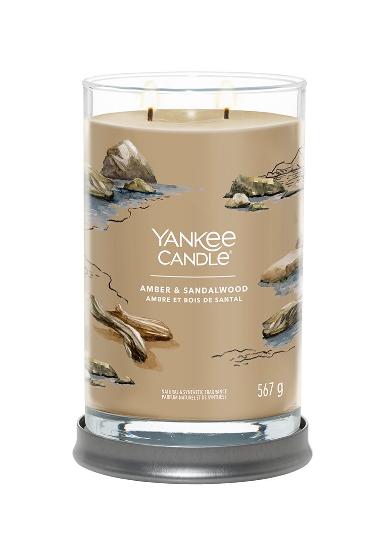 Yankee Candle en un frasco de vidrio transparente, con fragancia de ámbar y sándalo. Etiqueta marrón con ilustraciones de piedras y madera flotante; diseño de dos mechas.