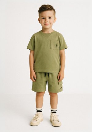 Kaki grøn bomulds t-shirt med lomme og logo, parret med matchende shorts og beige sneakers med sorte og hvide stribede sokker.