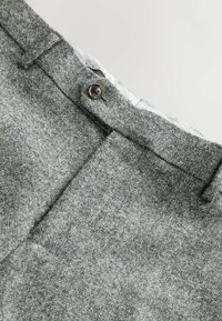 Grey textured trousers with a subtle weave, featuring a single button closure and sharp creases along the front, highlighting tailored design.