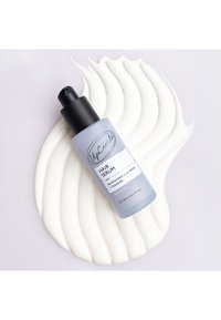 Hårserum i en frostad ljusblå flaska med svart pumpkork, placerad på en virvlande vit krämig textur.