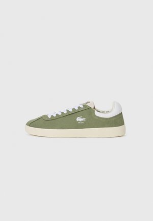 Green canvas sneakers with white laces and a white heel cap. Features a Lacoste logo in white. Classic low-top silhouette and rubber sole.