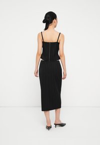 Svart, striped to-delt sett med en tettsittende topp med justerbare stropper og et langt, rett skjørt. Jevn stofftekstur.