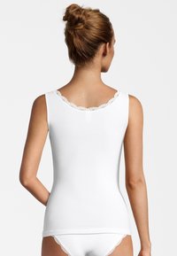 Top cortissimo bianco a costine con bordo in pizzo sullo scollo. Design aderente con bretelle larghe e texture liscia. Abbinato a biancheria intima bianca.
