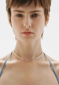 Collar de plata con un diseño elegante y minimalista. Presenta un acento metálico central y una superficie lisa y reflectante.