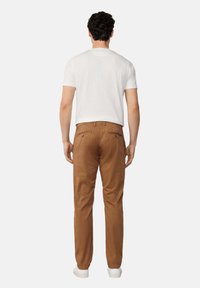 Pantaloni marroni da uomo con una texture liscia, tasche posteriori e una vestibilità comoda, abbinati a una t-shirt bianca a maniche corte.