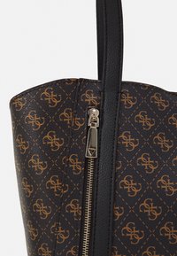 Gros plan sur un sac à main marron foncé avec un motif monogramme beige, une sangle verticale noire et une tirette en métal argenté.