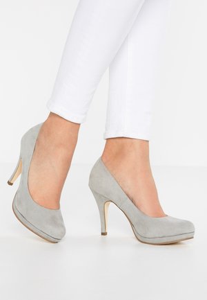 Chaussures à talons hauts en suède gris avec un bout arrondi, présentant une texture lisse et un talon fin de 10 cm. Portées avec un pantalon blanc court.