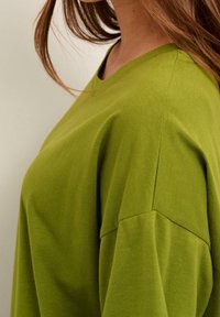 Olivgrön t-shirt med rund halsringning, korta ärmar och en avslappnad passform. Tillverkad av mjuk bomull, med en slät yta och sömsatta detaljer.