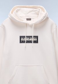 Sudadera con capucha en color crema claro, fabricada en tejido suave. Presenta un logotipo impreso en negro en la parte delantera y un bolsillo tipo canguro. Incluye cordones ajustables.