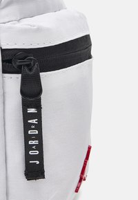 White fabric backpack with textured surface, black zipper, and a branded tag. Features a red accent detail on the side.