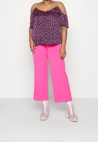 Haut noir avec imprimé girafe rose, épaules dénudées et bretelles en chaîne argentée ; assorti à un pantalon large rose vif et des talons compensés pailletés.