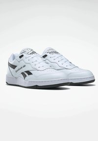 White Reebok sneakers featuring a smooth leather upper, black accents, perforated toe detail, and a cushioned sole.