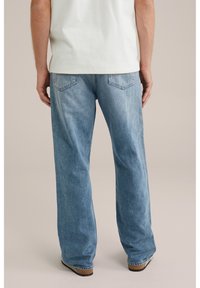 Lichtblauwe denim jeans met een recht gesneden ontwerp, met achterzakken en een zachte, gestructureerde afwerking. Draagt met een wit shirt.