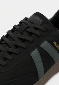 Mustad mustad tennisjalad, millel on tekstuurne pind, hallid triibud ja mustad paelad, kerge polsterdatud krae ning pruun kummist tallaga, millel on mustriga tallad.