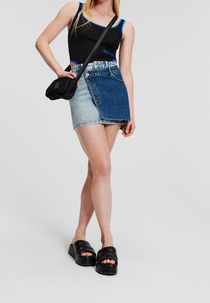 Ung kvinde iført en sort og blå ærmeløs top, halv lys og halv mørk denim nederdel, sort skuldertaske og sorte platformsandaler.