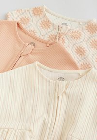 Trois bodies pour bébé à col rond, avec des imprimés de soleil pêche, un uni pêche, et un crème à rayures pêche, disposés en chevauchement sur une surface plane.