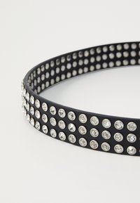 Cintura nera caratterizzata da strass tondi distribuiti uniformemente in montature argentate lungo tutta la lunghezza. Texture liscia, con forma piatta e design minimalista.