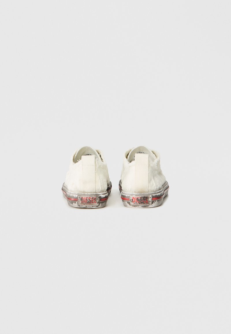 Un par de zapatillas de lona blancas gastadas con bordes deshilachados y logotipos en negro y rojo de "DIESEL" en las suelas de goma sucias, vistas desde la parte trasera.
