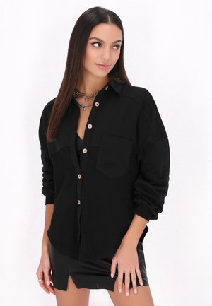 Camicia nera con bottoni, realizzata in un tessuto testurizzato, con una tasca sul petto, maniche arrotolate e bottoni in legno.