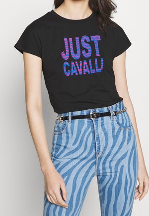 Kobieta ubrana w czarny krótki T-shirt z kolorowym napisem "JUST CAVALLI" oraz spodnie z wysokim stanem w niebieskie paski zebry i czarny pasek.
