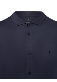 Marineblaues Poloshirt mit strukturiertem Finish, zwei Knöpfen, einem Kragen und einem kleinen Logo auf der linken Seite. Der Stoff wirkt weich und leicht.