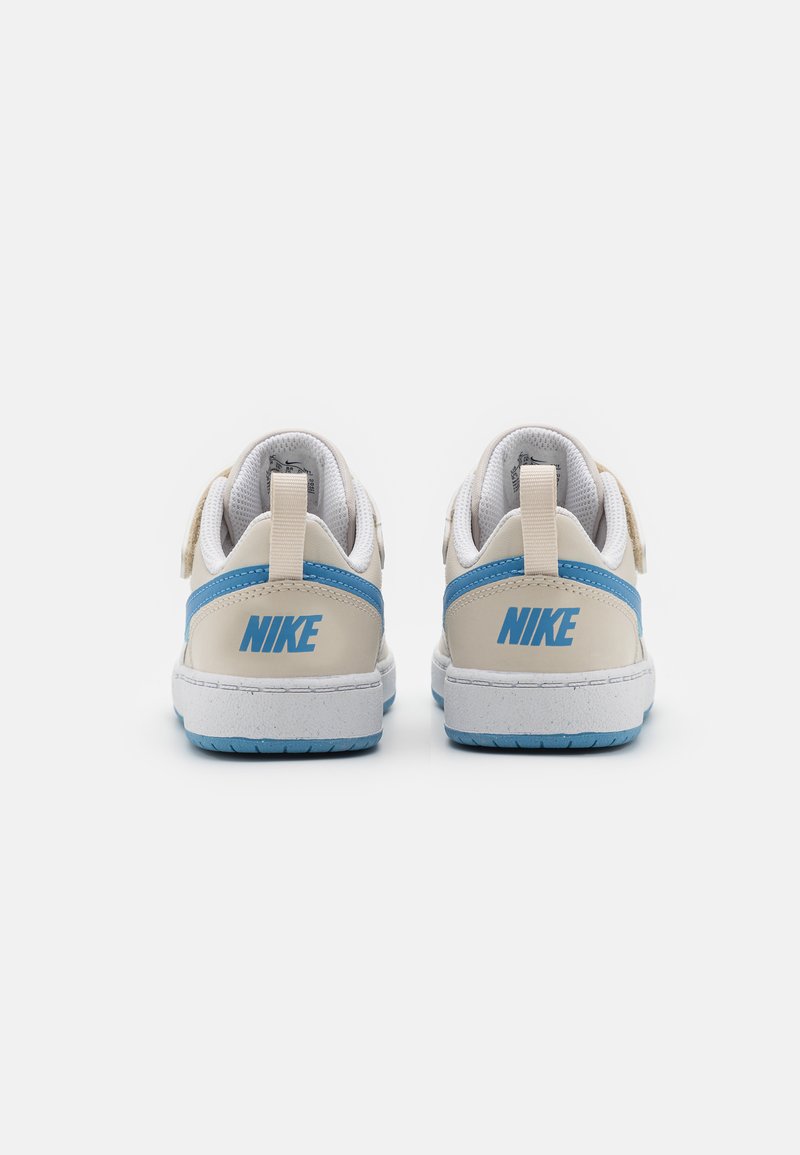 Des baskets blanches avec des accents bleu clair et un swoosh beige. Elles présentent un dessus texturé et une semelle en caoutchouc avec un logo à l'arrière.