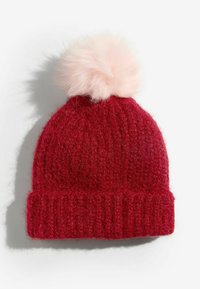 Punane kootud beanie, millel on soonikserv ja pehme roosa kunstkarvune pom-pom peal. Pehme tekstuur ja soe disain, mis sobib külma ilma jaoks.