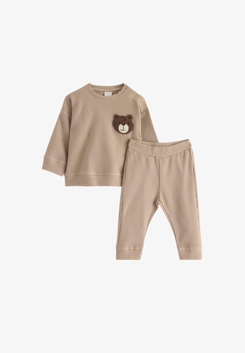 Beiges Baumwollstrick-Zweiteiler-Outfit mit einem langärmeligen Oberteil, das ein Bären-Patch aufweist, und passenden schmal zulaufenden Hosen mit elastischem Taillenbund.