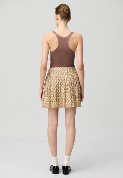 Top de tirantes marrón con relleno, de espalda redonda, combinado con una falda pleated beige con un estampado floral y zapatos negros con calcetines de crema.