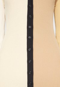 Gros plan sur un tissu en maille côtelée avec une bande verticale de boutons noirs divisant les panneaux crème et beige.