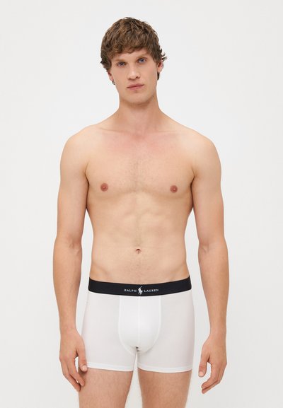 Beli boxer kratke hlače iz raztegljivega blaga z črnim elastičnim pasom, na katerem je napis "RALPH LAUREN". Gladka tekstura, oprijet dizajn.