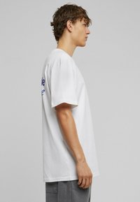 Hvid bomulds-T-shirt med korte ærmer, rund hals, med blå tekst på ryggen, afslappet pasform og glat tekstur.
