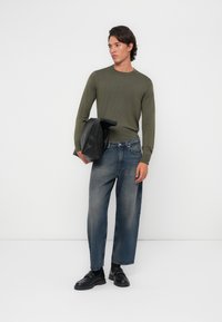 Camisa verde de manga larga, vaqueros azules holgados, zapatos negros sin cordones, sosteniendo una chaqueta de cuero negra. Diseño sencillo, textura suave, estilo casual.