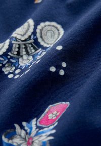 Detailný záber modrej látky s bielymi a ružovými kvetinovými a kruhovými vzormi, zobrazujúci textúru a šité detaily.