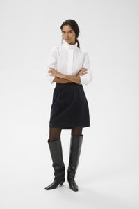 Fehér galléros ing, sötét kordbársony szoknya és térdig érő fekete bőr csizma. A szoknya pliszírozott, a csizma hegyes orrú.